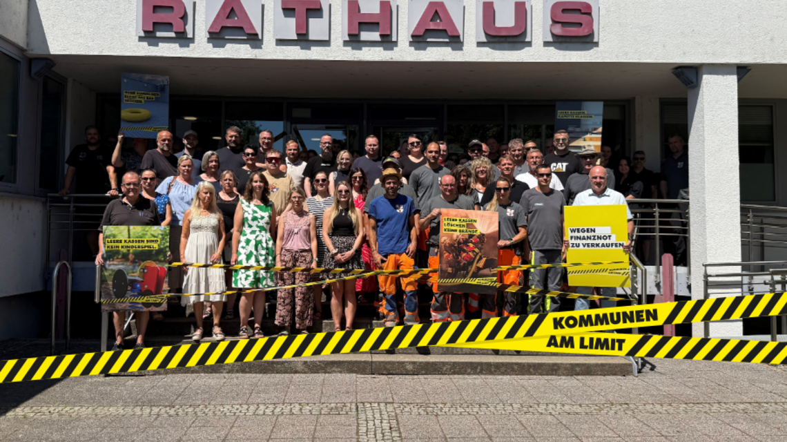 Bild zeigt Mitarbeiter/-innen mit Bürgermeister Wolfram Lang vor dem Rathaus der Gemeinde Schmelz anlässlich der "Kommunen am Limit" Aktion am 22.06.2026